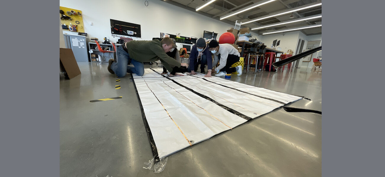 Four male students kneel on the floor working on a project.