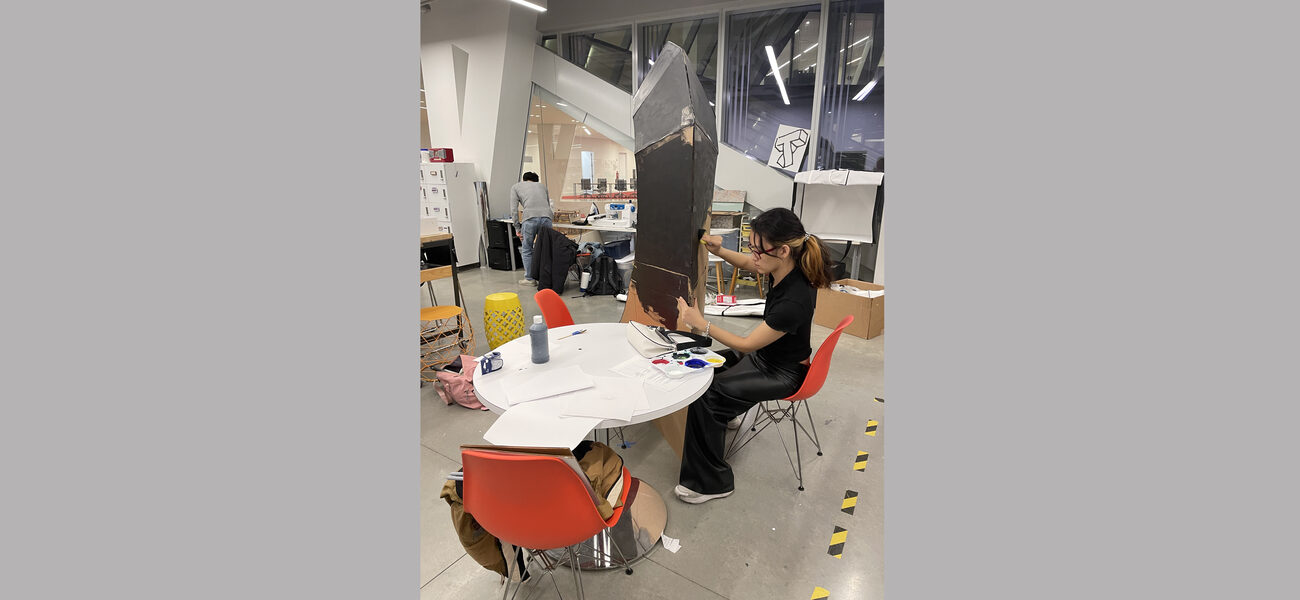 A female student sits at a table working on a large installation..