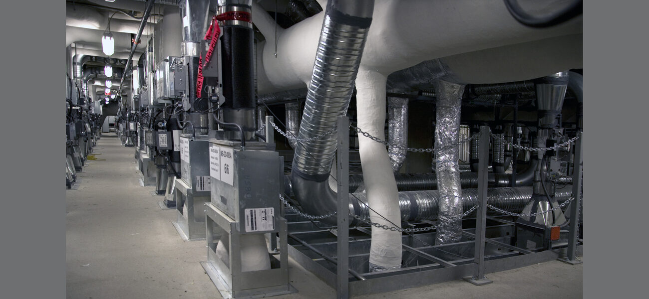 A narrow walkway with floor-to-ceiling vents and ducts on the right