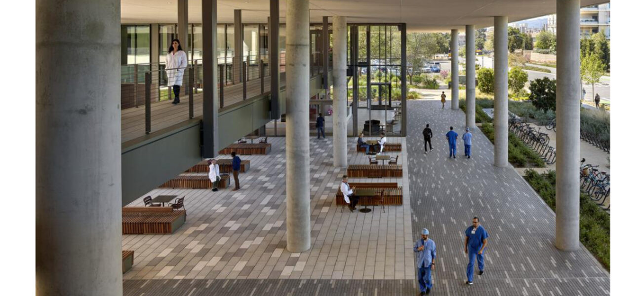 People walk through a large covered, outdoor space with tables and chairs.