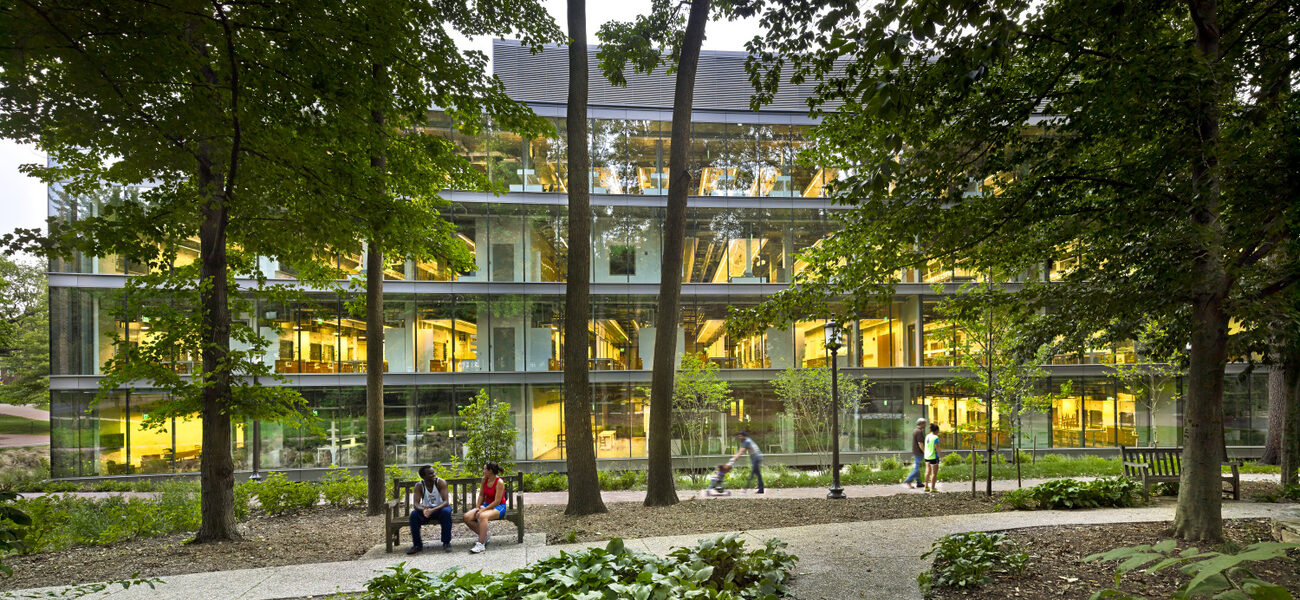 Exterior of a large building sheathed in glass with trees in the foreground