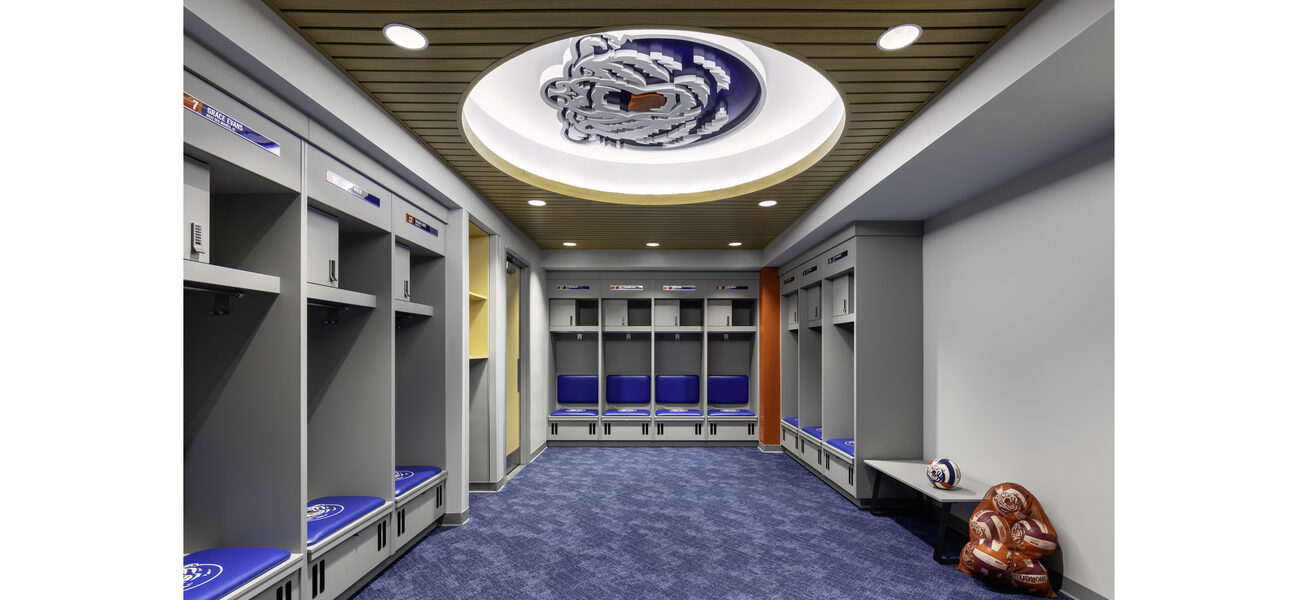 A long room with a carpet on the floor and the walls lined with padded seats and lockers