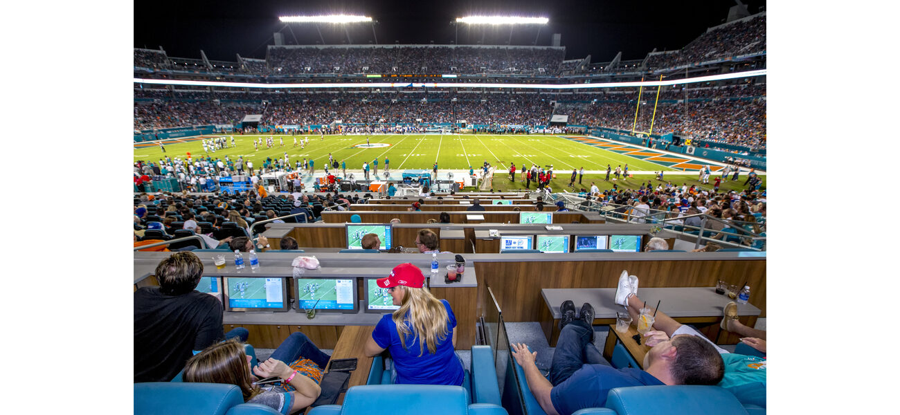 Two men and two women recline in comfortable seats in a section of a football stadium.