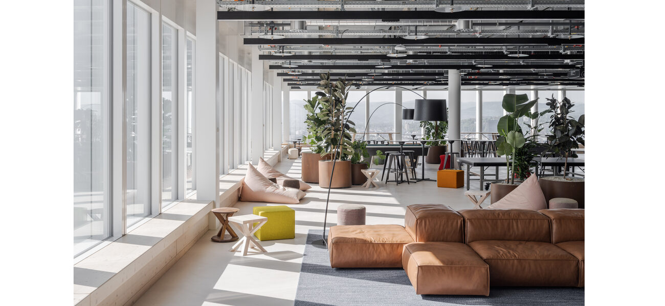 Large room with a wall of windows, upholstered couches and several tables with chairs.