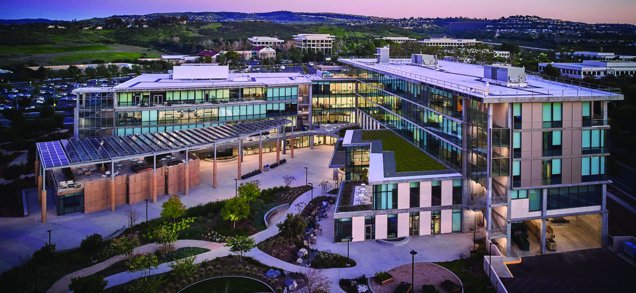 Exterior of a large building wwit htwo wings, wit hwalkways in the front and mounjtains behind