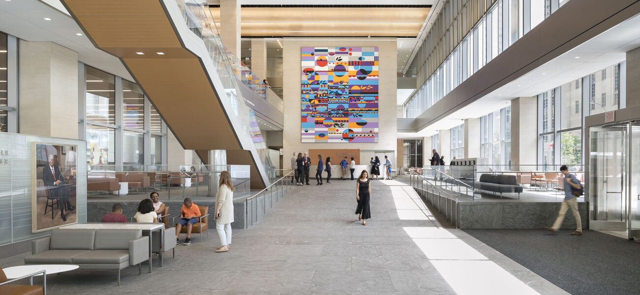 Large interior space with some people sitting on soft furniture while others walk through the space.