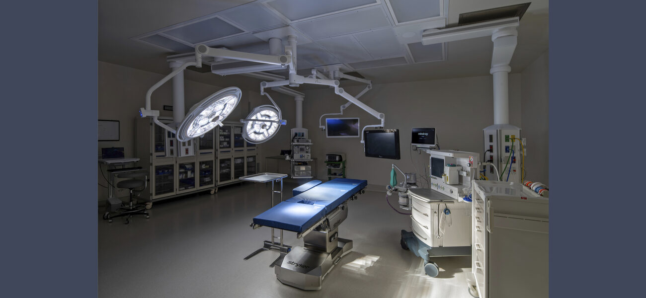 And operating table with bright lights above it and two computer monitors overhead.