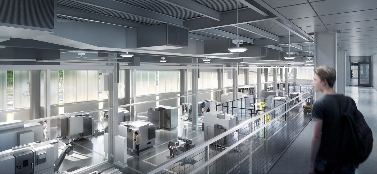 A white male stands on a walkway overlooking a large room full of machinery.