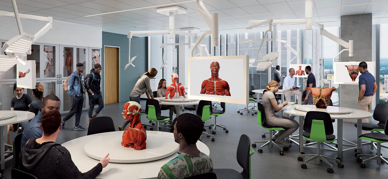 Male and female collge students sit at round tables, each of which has an anatomical model in the center