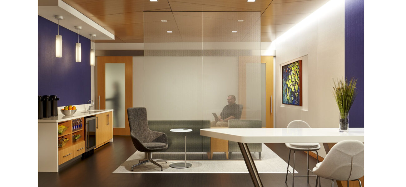 A man sits on a couch in a room that also has a coffee bar, a table and chairs.