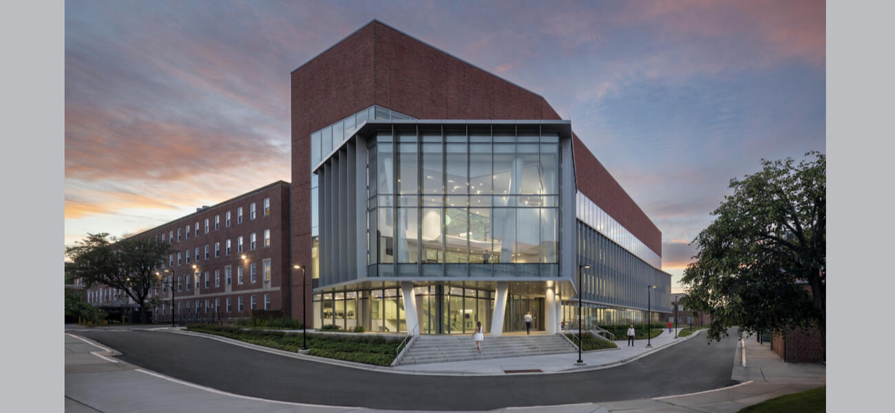 Large briuck building with many large windowns in the front and smaller windows lining the side.