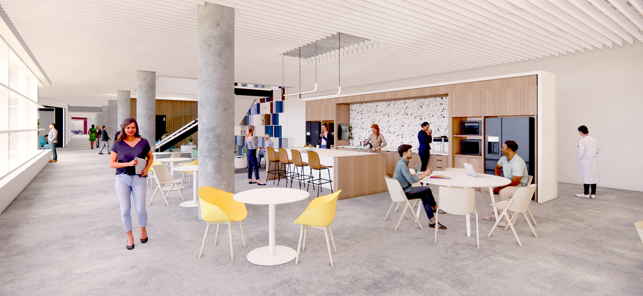 Two men sit at a round table in a large space. A woman stands at a bar while two women stand behind the bar.