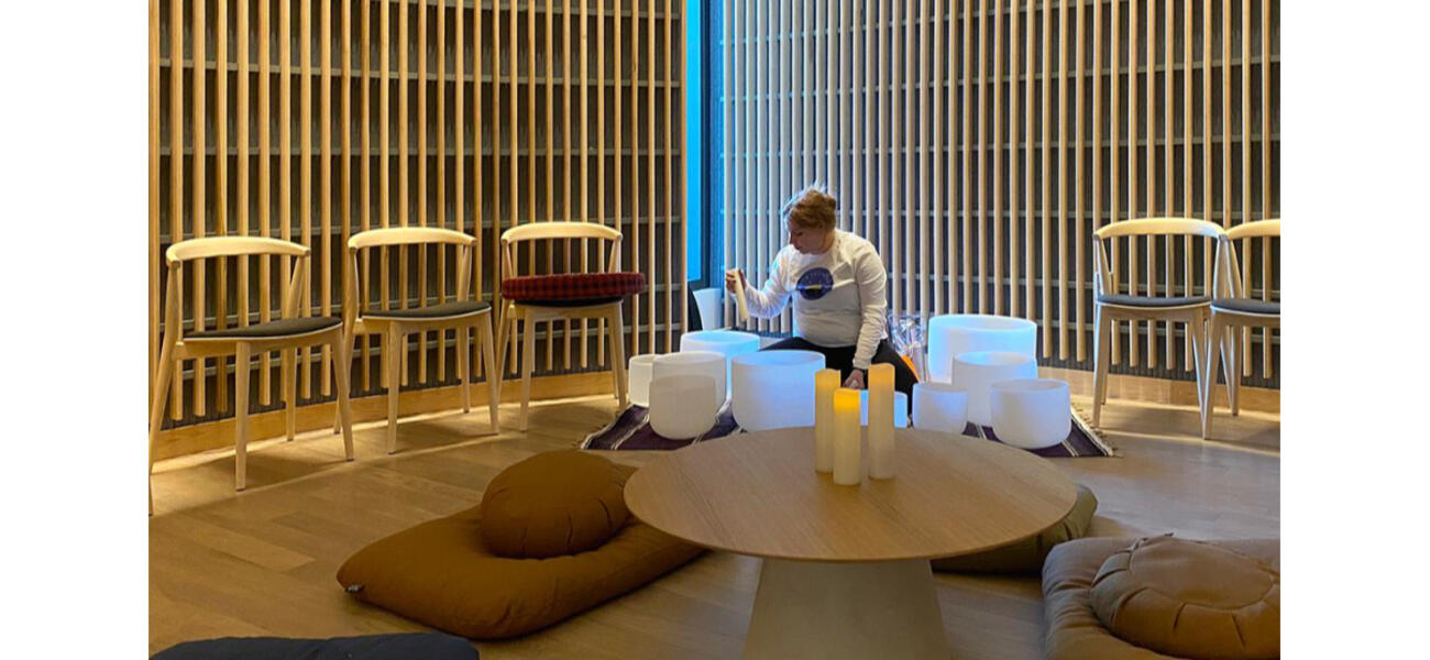 A man sits alone in a room where the walls are lined with wooden slats. Candles burn on the table in front of him.