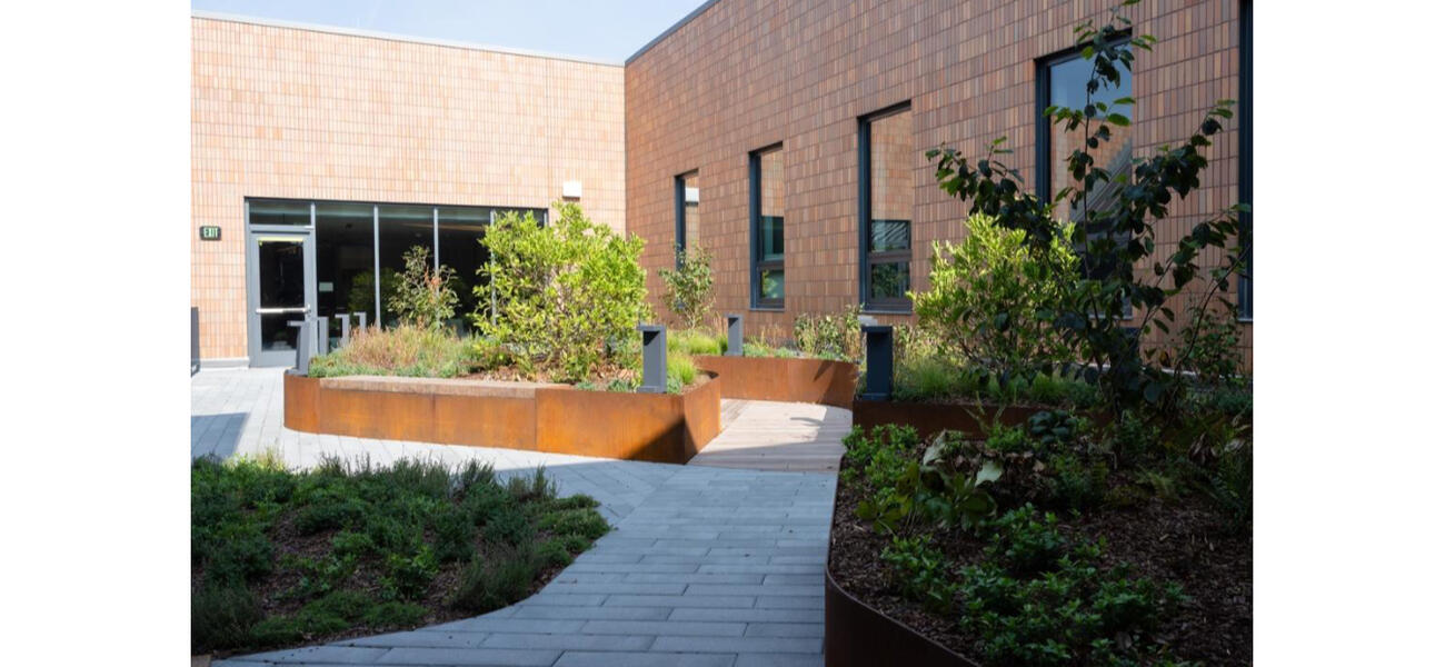 A brick path winds around plantings outside a brick building.