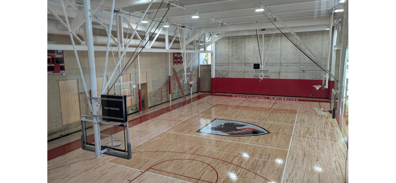 A basketball court with wooden floor and baskets hanging from the ceiling on either 