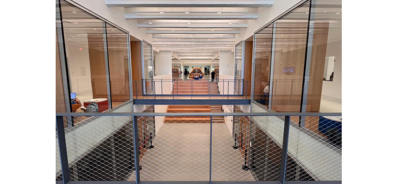 A wide corridor with two floors of room on either side, all sided in glass.