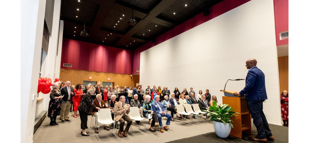 A man stands at a podium in front of a roomful of men and women.