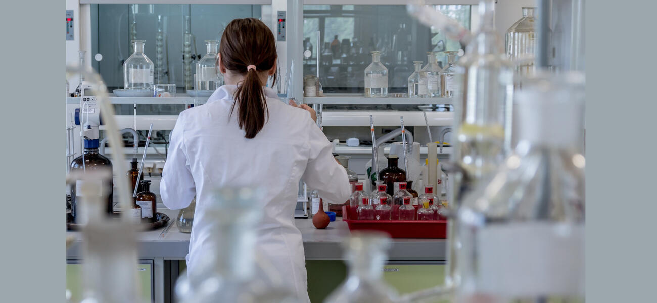 A woman in a lab coat works at a cluttered lab bench.
