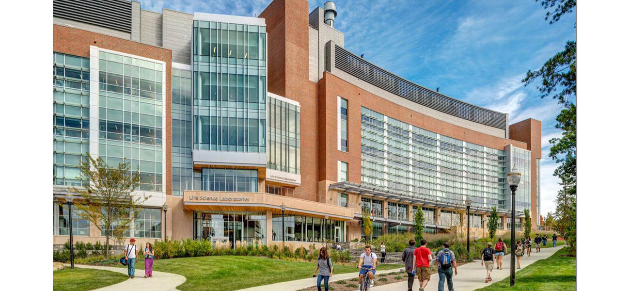 Exterior of a long, curved, building sided in brick and glass. People walk on a sidewalk in front.