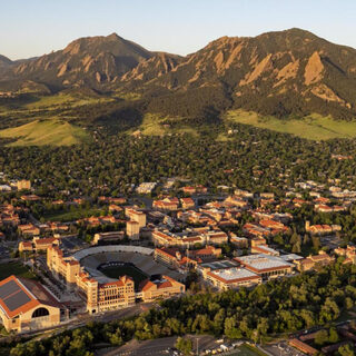 Aereal view of a campus with many buildings and an athletic stadium with a row of mountains behind it