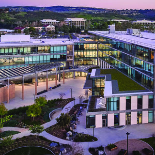 Exterior of a large building wwit htwo wings, wit hwalkways in the front and mounjtains behind