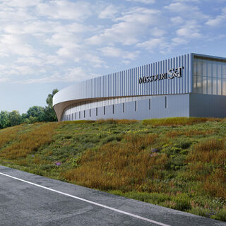 Large, curved, metalic building by the side of a highway