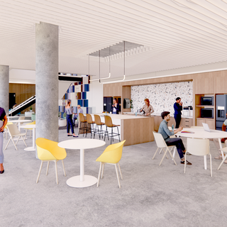 Two men sit at a round table in a large space. A woman stands at a bar while two women stand behind the bar.