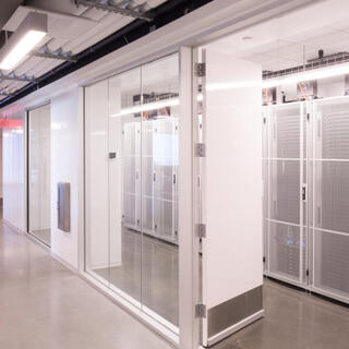 A stark, brightly-lit hallway lined with glass behind which are massive banks of computers