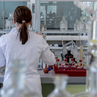 A woman in a lab coat works at a cluttered lab bench.